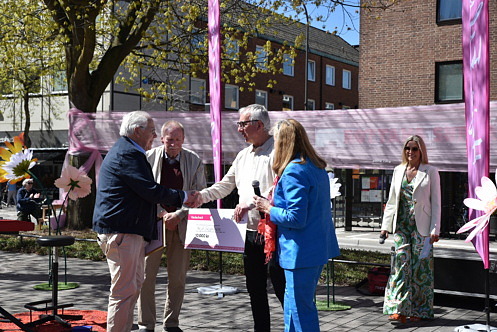 Fem personer st&aring;r p&aring; en scen p&aring; Stora torg i Esl&ouml;v under en prisutdelning i str&aring;lande solsken. En kvinna i bl&aring; kostym h&aring;ller tal i mikrofon och en man i vit tr&ouml;ja skakar hand med pristagaren och l&auml;mnar &ouml;ver prischecken. tv&aring; personer bredvid h&aring;ller ett diplom och en stor prischeck.