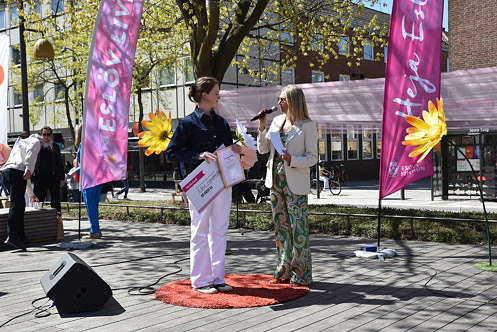 Tv&aring; personer st&aring;r p&aring; en scen p&aring; Stora torg i Esl&ouml;v under en prisutdelning i str&aring;lande solsken. En kvinna i vit kavaj intervjuar pristagaren medan pristagaren h&aring;ller ett diplom och en stor prischeck.
