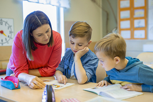 två förskolebarn, pojkar, sitter vid ett bord och talar med en kvinnlig förskolelärare