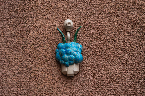 Liten skulptur föreställande en stiliserad mänsklig figur monterad på en fasad i stadsmiljö. Skulpturen är en del av en serie konstverk som är utplacerade runt kvarteret Gjutaren i Eslöv.