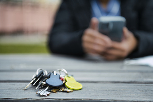 Hemtjänstens nyckelknippa på ett bord med en hemtjänstpersonal med telefon i bakgrunden.