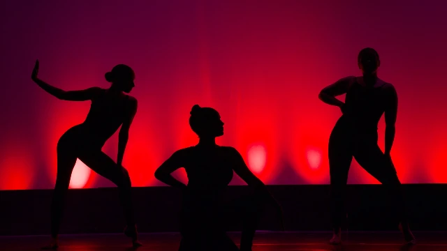 tre kvinnor som dansar på en scen i rött ljus