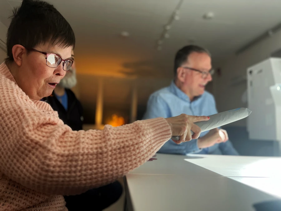 En kvinna sitter vid borde och h&aring;ller i ett f&ouml;rem&aring;l som hj&auml;lper henne att interagera med bilderna som projiceras p&aring; bordet. 