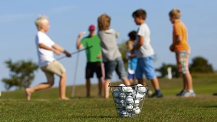 En korg med golfbollar och barn med golfklubbor i bakgrunden