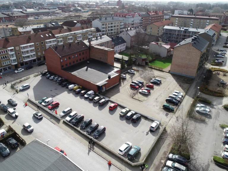 Drönarbild över kvarteret som till stor del består av en parkeringsplats. Omkringliggande gator och hus runt om.