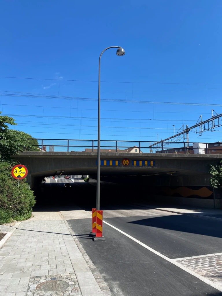 Lyktstople står mitt i cykelbana. Järnvägsbro i bakgrunden.