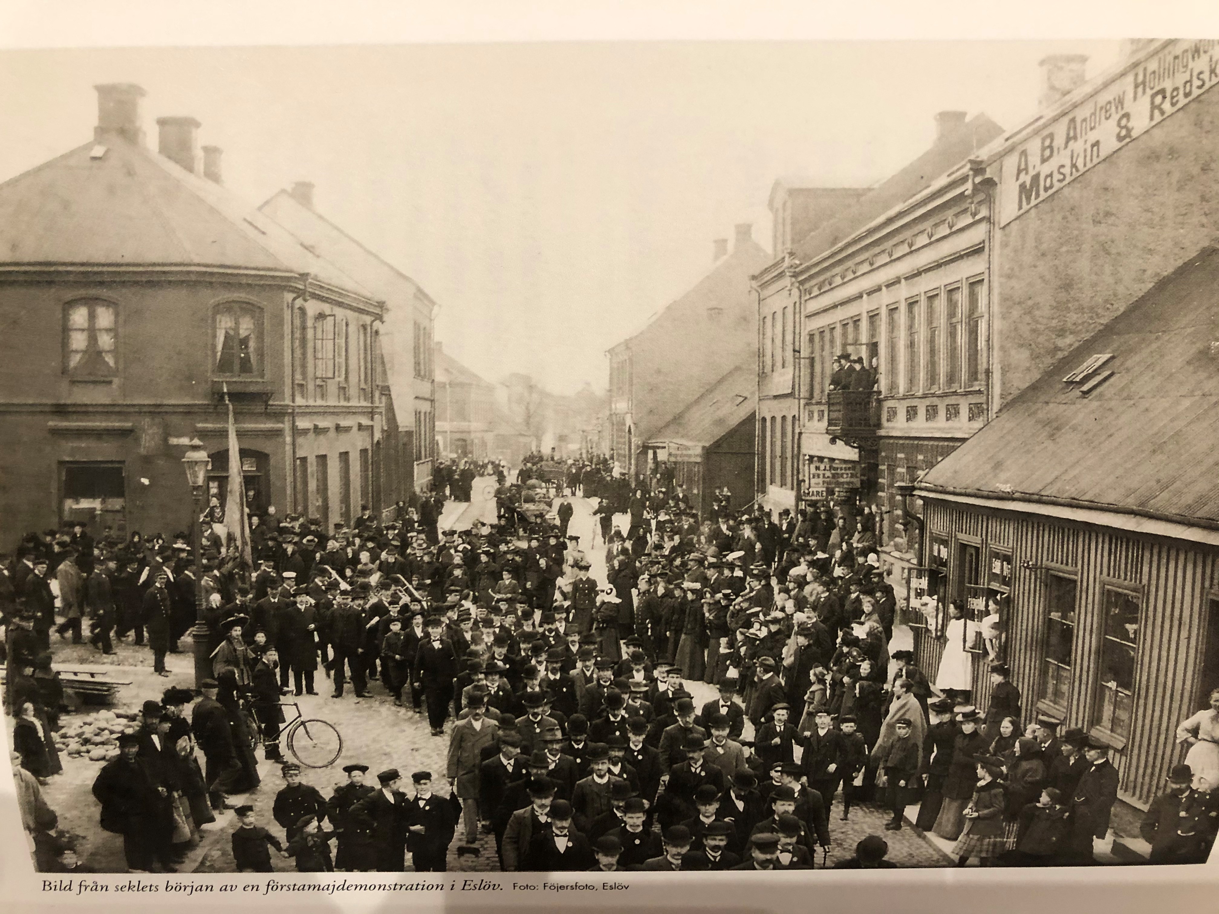 Bild fr&aring;n seklets b&ouml;rjan av en f&ouml;rstamajdemonstration i Esl&ouml;v. Bilden &auml;r tagen uppifr&aring;n j&auml;rnv&auml;gen och visar &Ouml;stergatan i v&auml;stlig riktning. Tr&auml;huset till h&ouml;ger &auml;r rivet, men inskriptionen p&aring; gaveln till stenhuset finns &auml;n idag. Foto: F&ouml;jers arkiv.