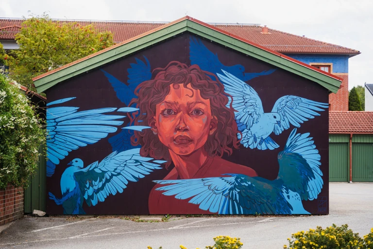 Färgstark muralmålning med ett stort porträtt målat över en hög husfasad. Konstverket använder starka färger och mjuka övergångar som skapar ett uttrycksfullt och levande motiv.