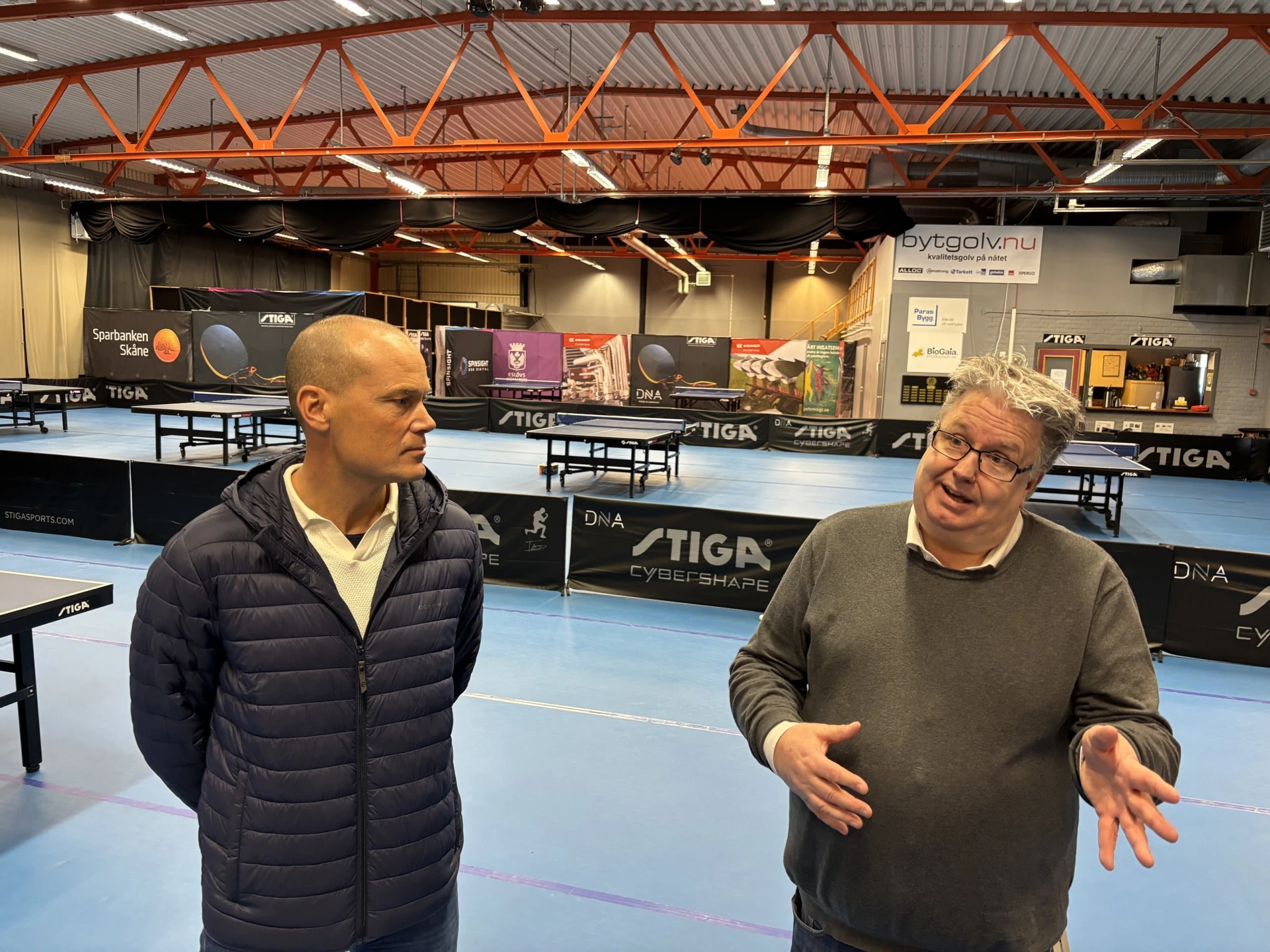 Två man samtalar i en bordtennishall