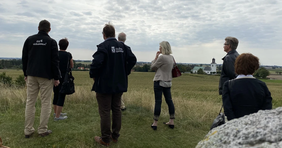 Sju personer med ryggen mot kameran blickar ut över Karaby backar