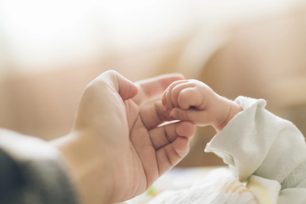 En liten bebishand håller i sin förälders finger