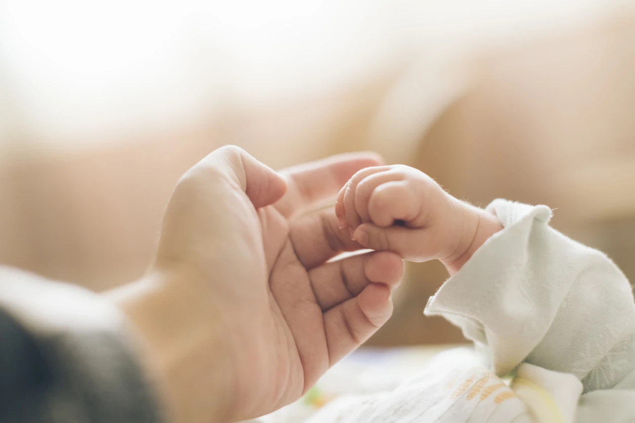 En liten bebishand håller i sin förälders finger
