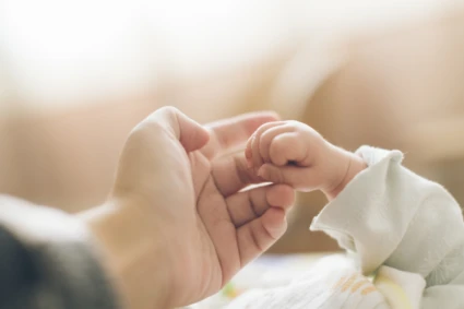 En liten bebishand håller i sin förälders finger