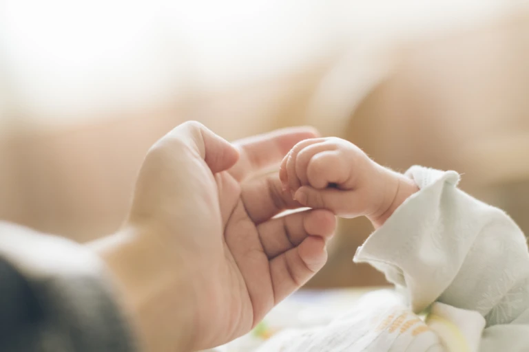 En liten bebishand håller i sin förälders finger