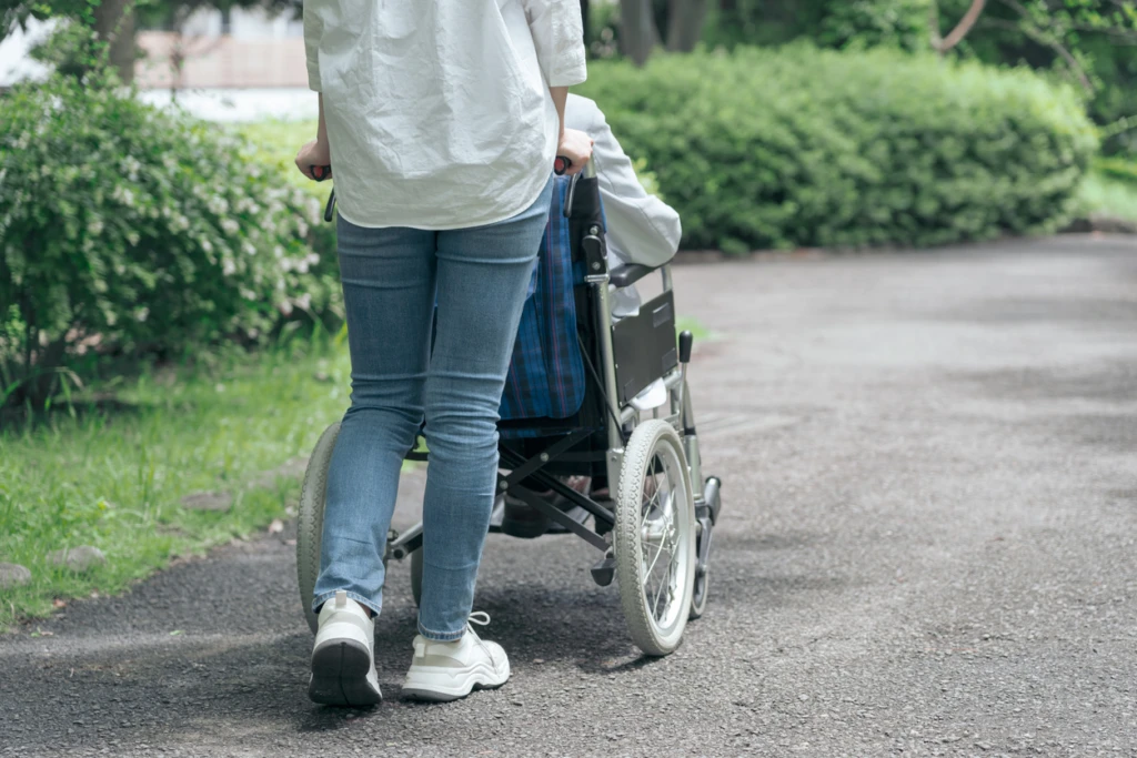 En kvinna är ute och går med någon i rullstol, man ser bara ryggen på kvinnan och rullstolen