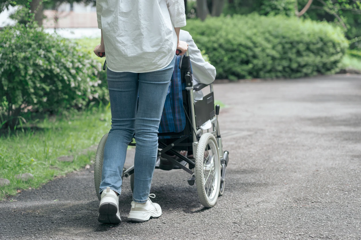 En kvinna är ute och går med någon i rullstol, man ser bara ryggen på kvinnan och rullstolen