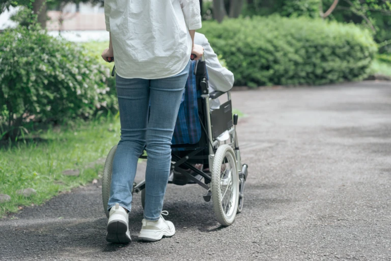 En kvinna är ute och går med någon i rullstol, man ser bara ryggen på kvinnan och rullstolen
