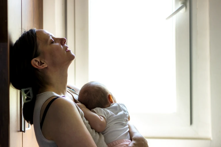 En trött mamma håller sitt spädbarn mot bröstet