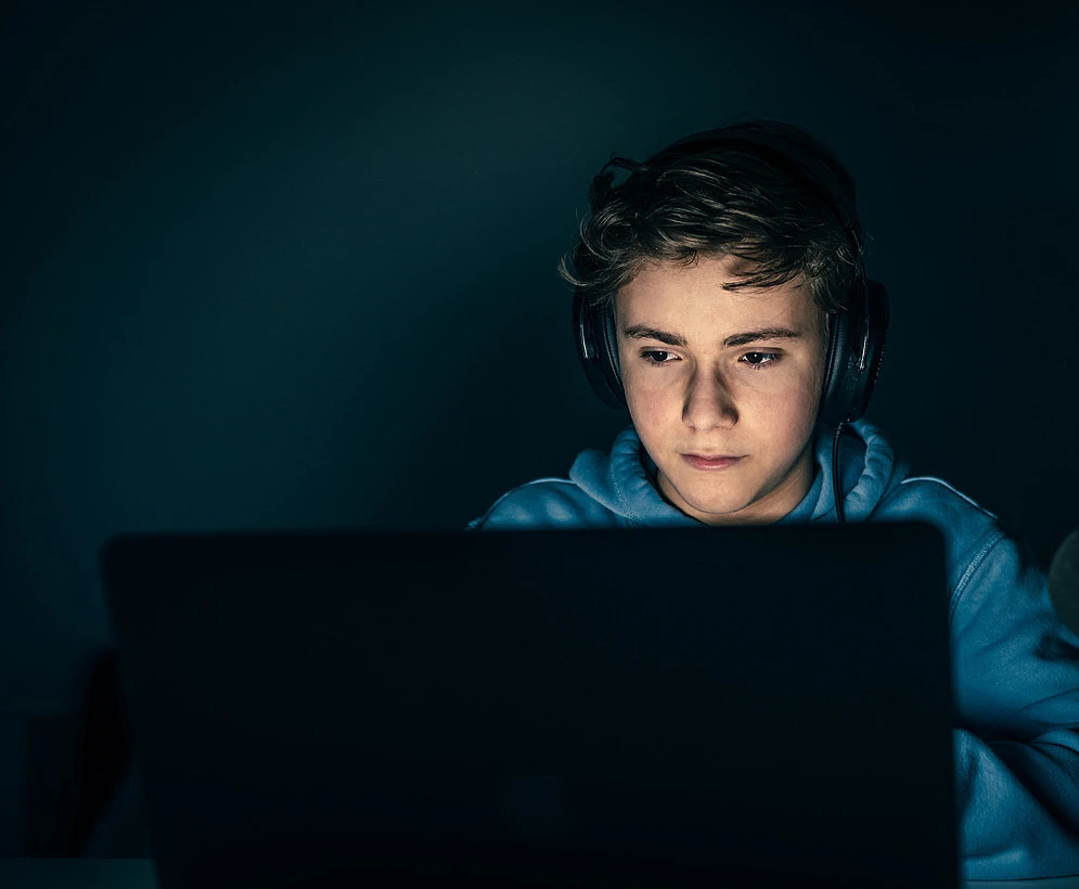 En ung kille sitter med headset och spelar datorspel