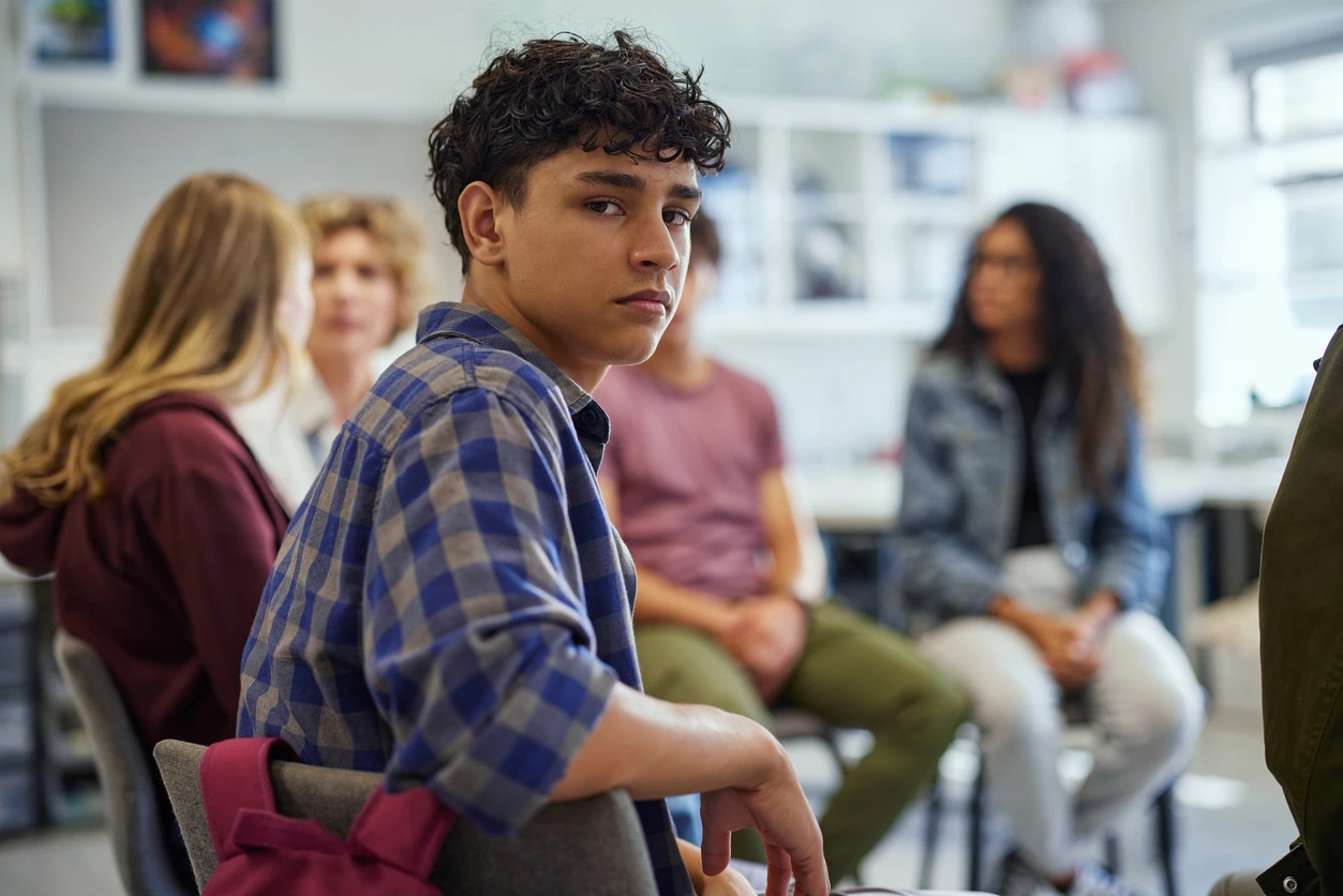 En tonårig kille sitter med klasskompisar och kollar in i kameran