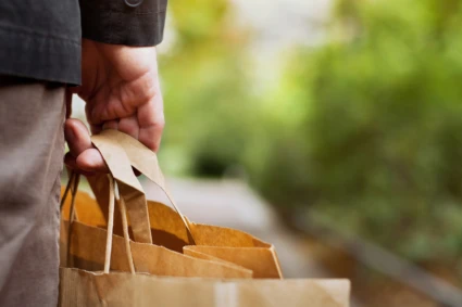 En hand som tillhör en äldre man håller i handtagen till en papperspåse