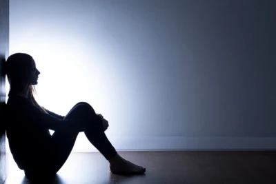 Ensam person som sitter lutade mot vägg med armarna runt benen.
