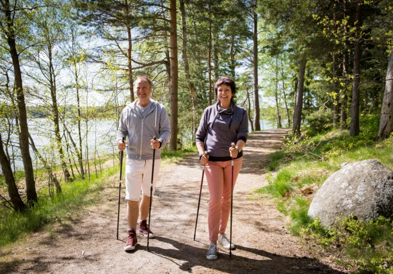 Man och kvinna går stavgång en solig sommardag i en skog.
