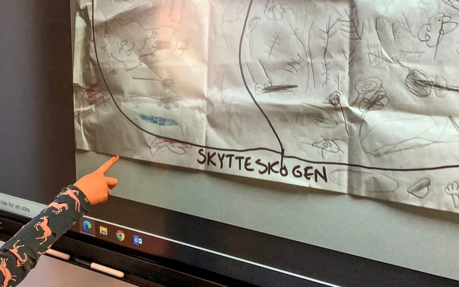 Ett barn pekar med sitt finger för att visa att karta över skogen som barnen har ritat.