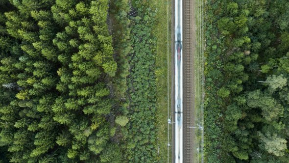 Drönarbild med tåg på stambanan lodrätt över bilden, gräs, buskar och träd runtomkring