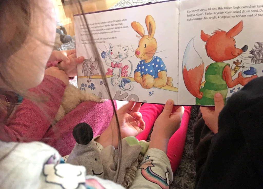 Barn tittar i en bok tillsammans med pedagog.