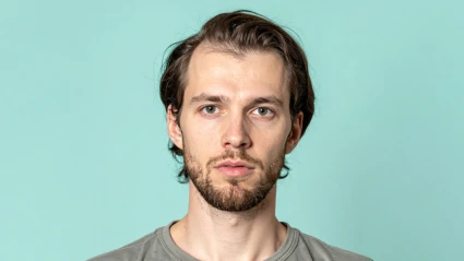 En person står framför en ljus turkos bakgrund. Personen har brunt hår och bär en grå t-shirt.