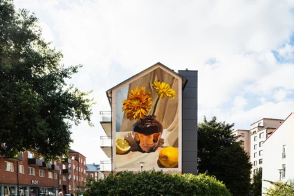 Muralmålning med en vas fylld av blommor och citroner i varma jordnära färger. Konstverket täcker en hög husgavel i centrala Eslöv.