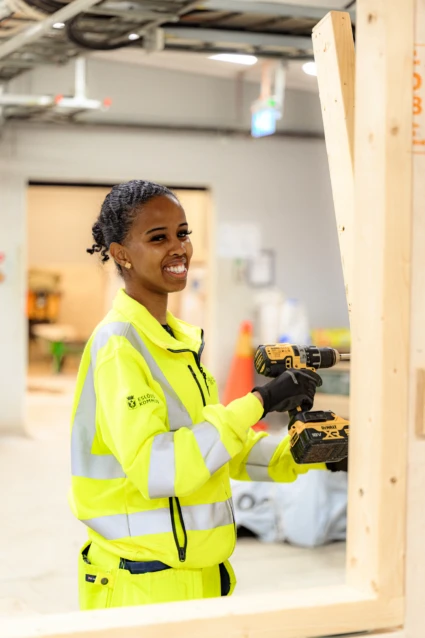 Tjej ler mot kameran med en borrmaskin
