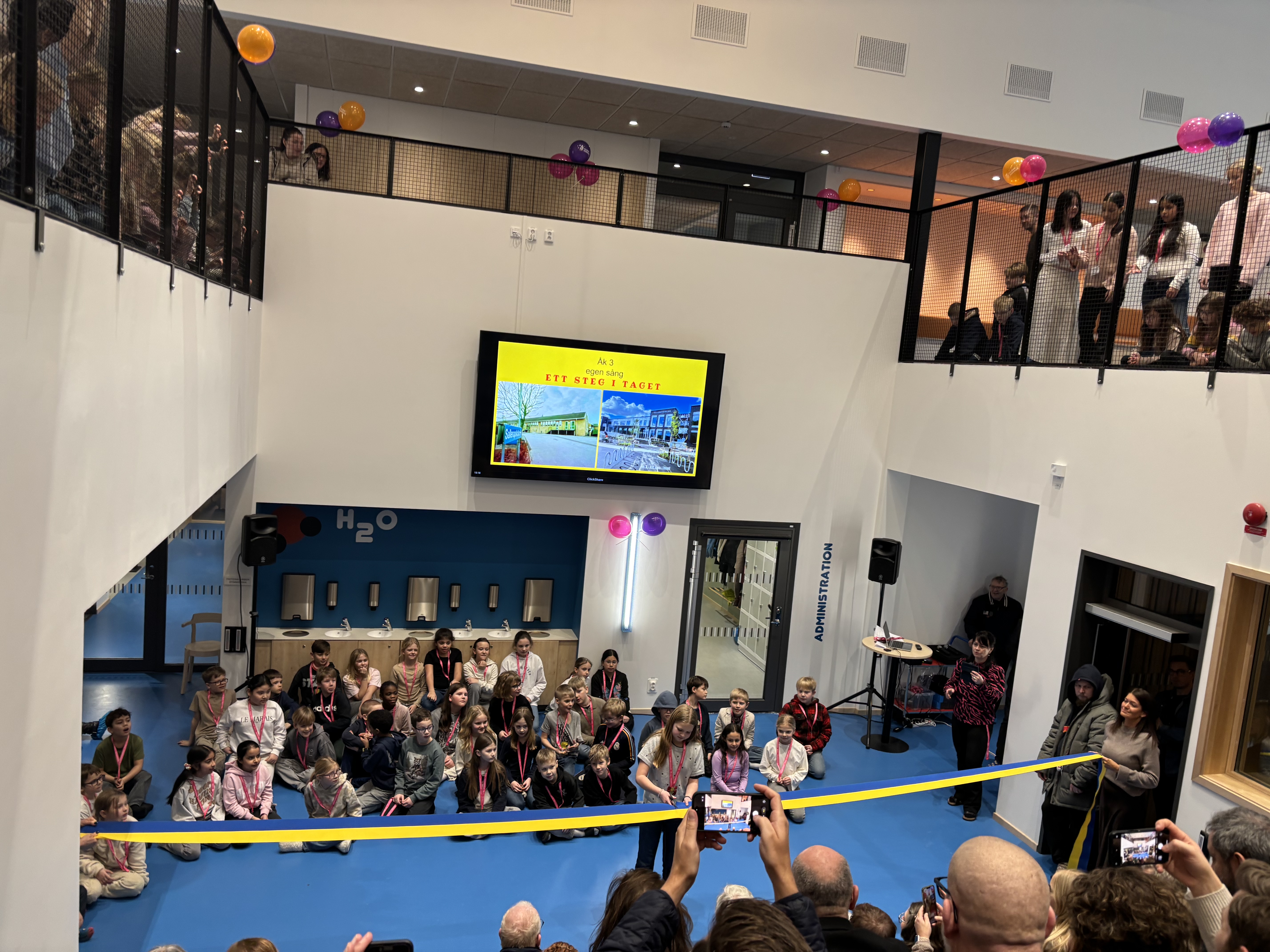 Inomhus milj&ouml; salleruppskolan, barn klipper av invigningsband. elever och l&auml;rare samlade runt