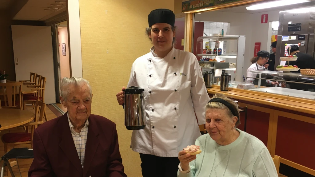 Stig och Elsa sitter vid bordet. anna-Karin står mellan dem med kaffekannan.