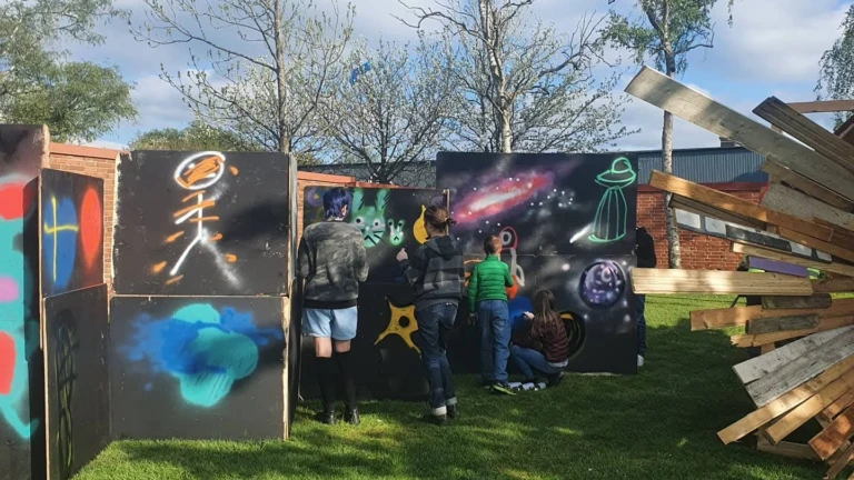 Fyra ungdomar står och målar graffiti på ett plank